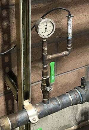 An old-style dial pressure gauge connected to piping near a pressure transmitter