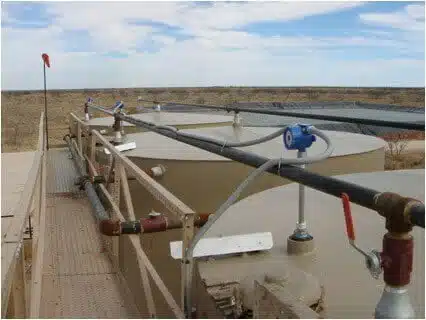 Large tan painted chemical tanks in the desert have level sensors installed on them.